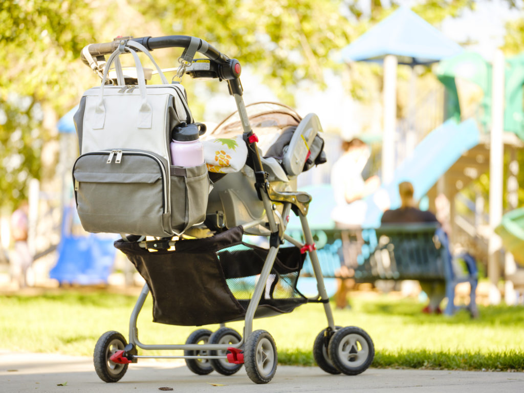 A baby stroller with a diaper bag at the park.